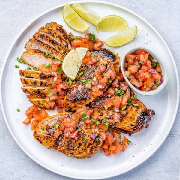 top view cooked jerk chicken breast on a plate with lime garnish and side of salsa