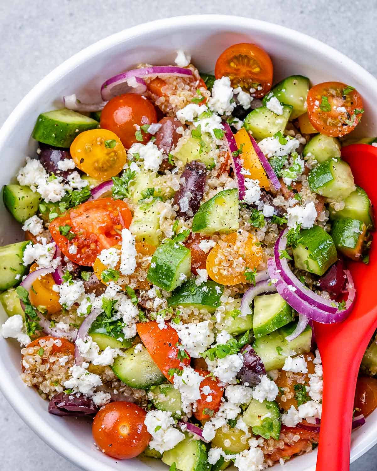 top view of quinoa salad in a white bowl with red spoon in it