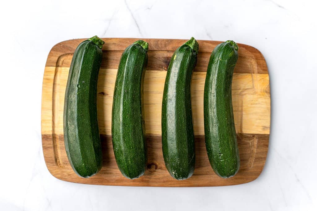 4 green zucchinis on a brown cutting board