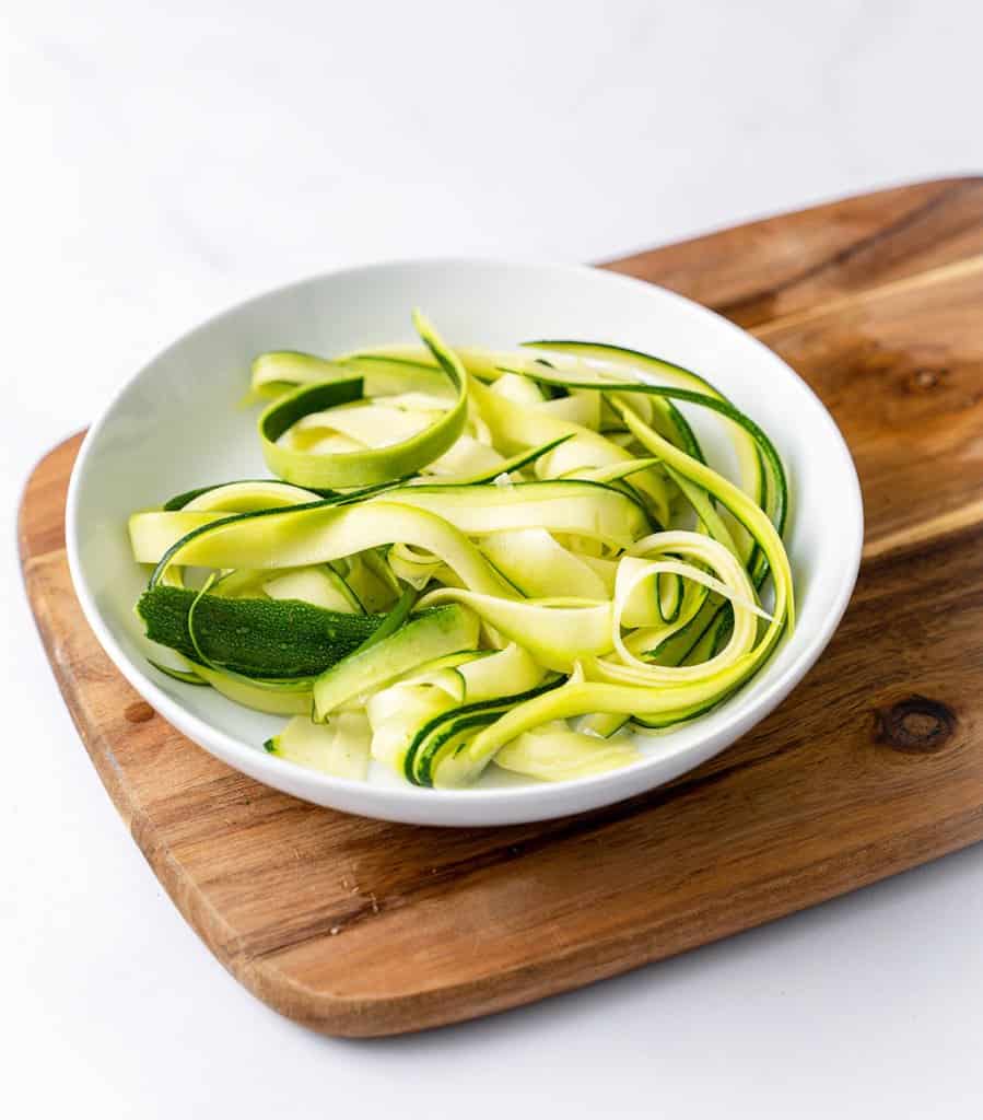 side shot of zoodles in a white plate over a brown cutting board
