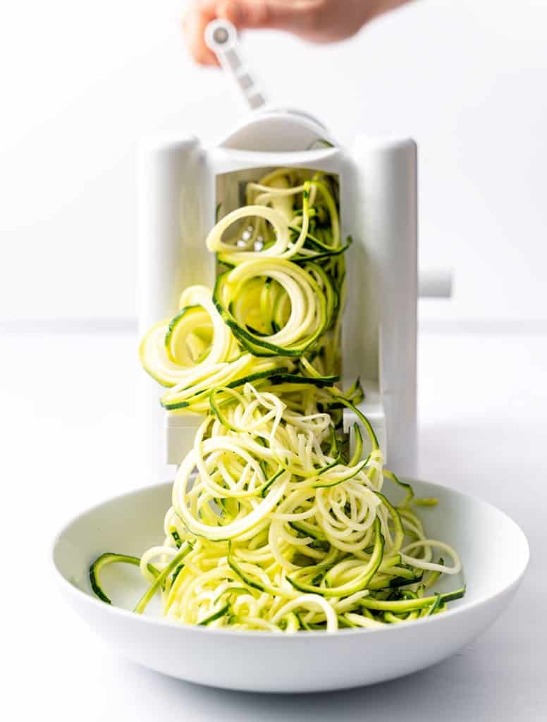 using spiralizer to make the zucchini noodles onto a white plate