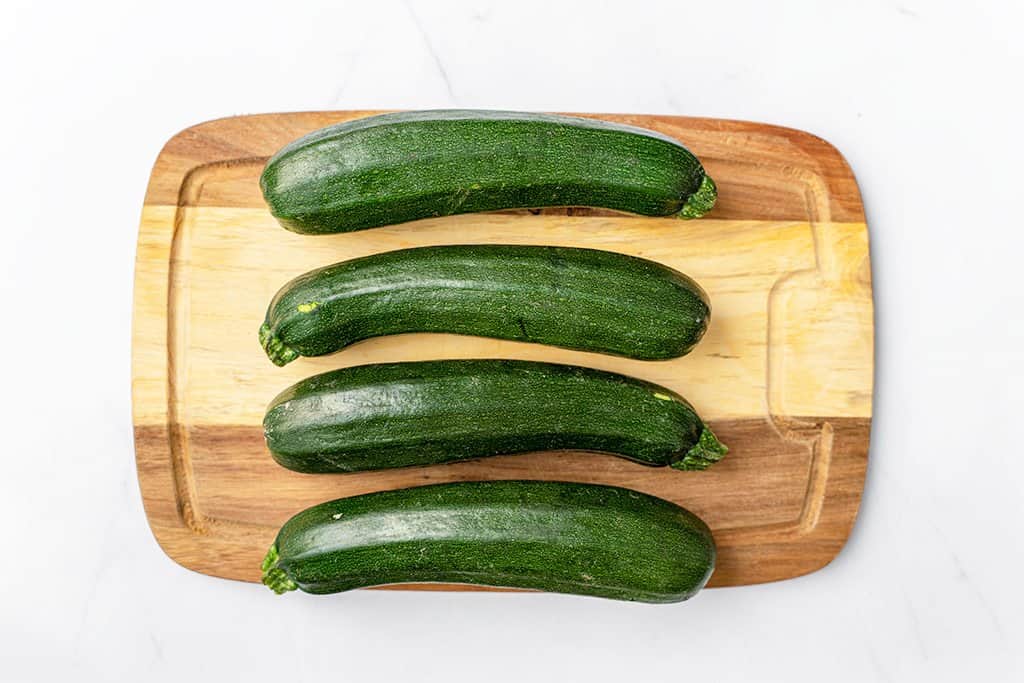 4 whole green zucchinis on a brown cutting board