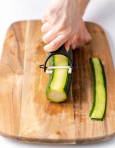 hand holding peeler and pealing a thin layer off zucchini