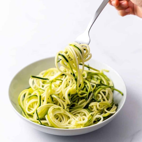 hand holding a fork grabbing zoodles from a white plate