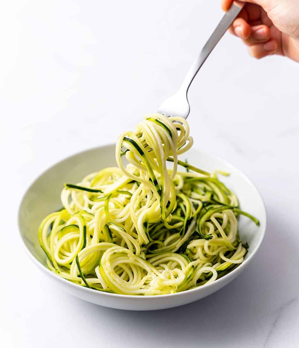 hand holding a fork grabbing zoodles from a white plate