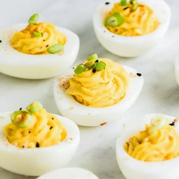 deviled eggs on a flat surface topped with green onions and sesame seeds.