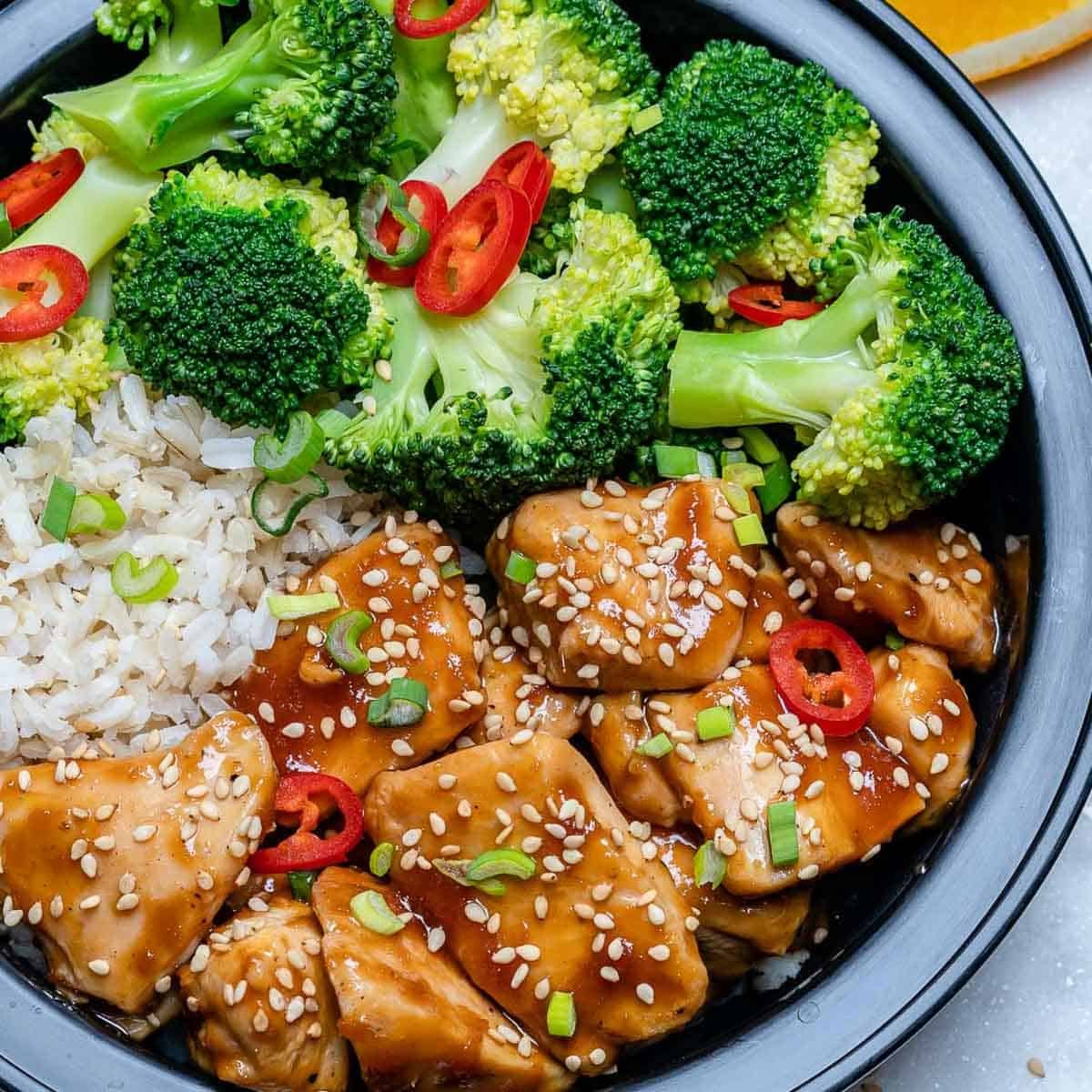meal prep bowl with chicken teriyaki, rice, broccoli, topped with sesame seeds.