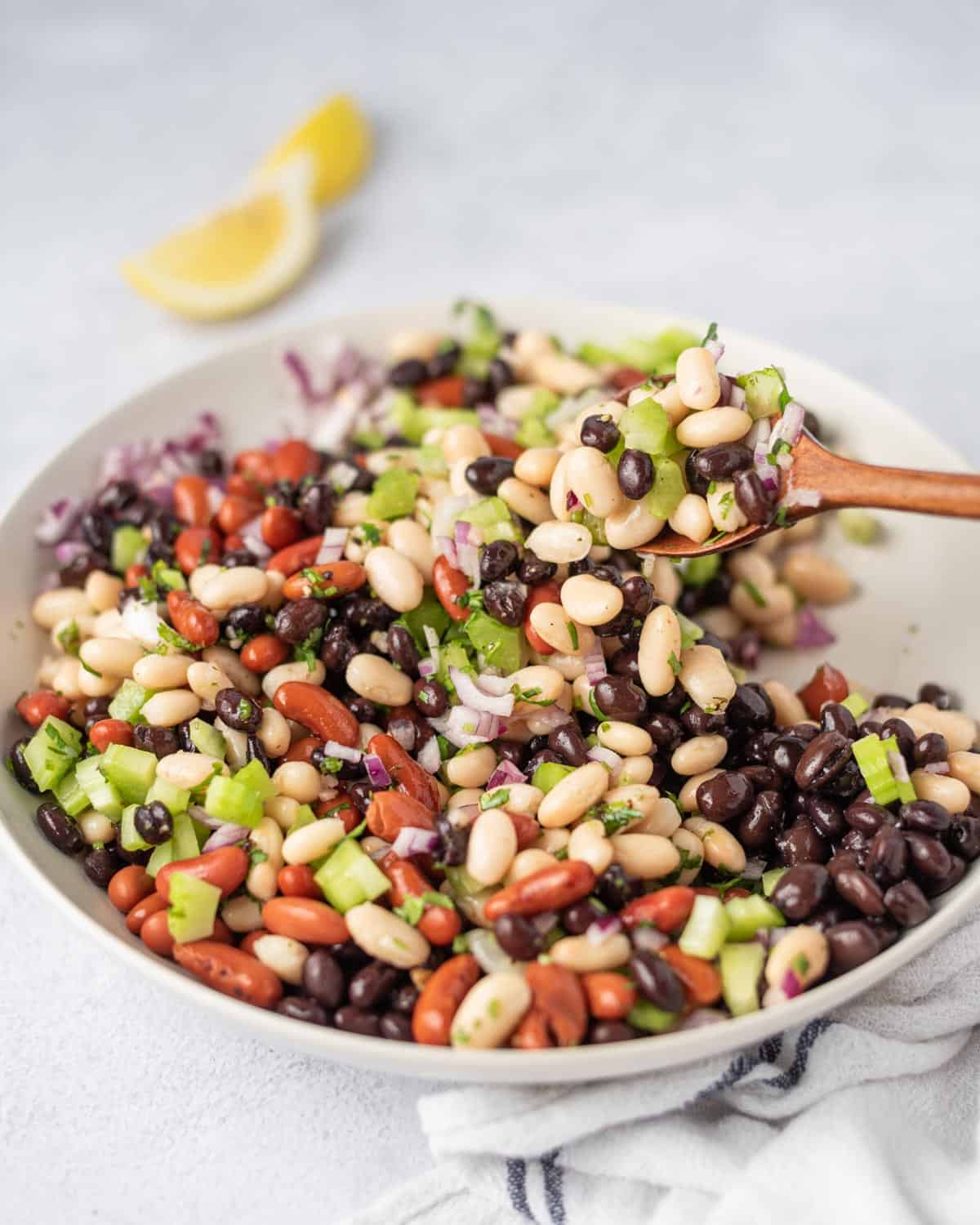 white bowl with three beans salad recipe and wooden spoon