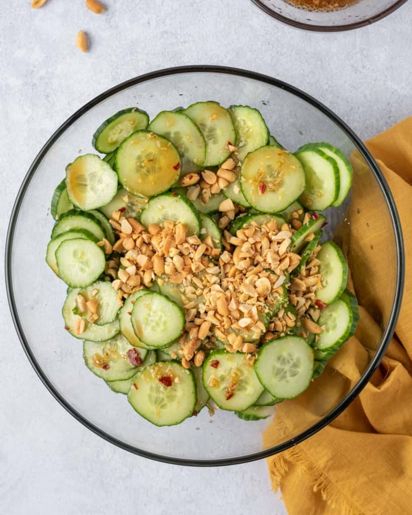 Crushed peanuts on top of sliced cucumber in a clear bowl.