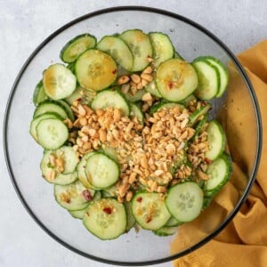 crushed peanuts added over cucumber salad in a clear bowl.