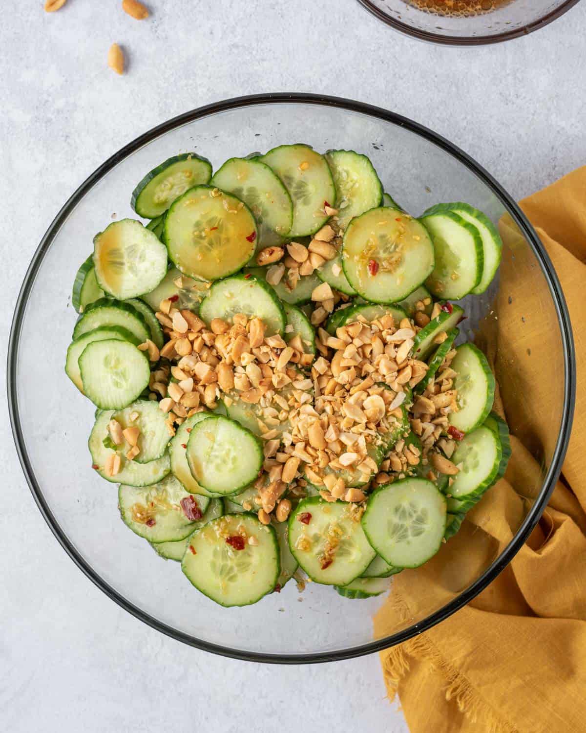 crushed peanuts added over cucumber salad in a clear bowl.