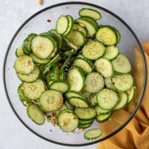 cucumber tossed in with dressing in a clear round bowl.