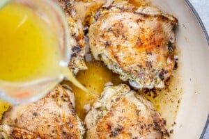 pouring chicken stock over thighs in skillet