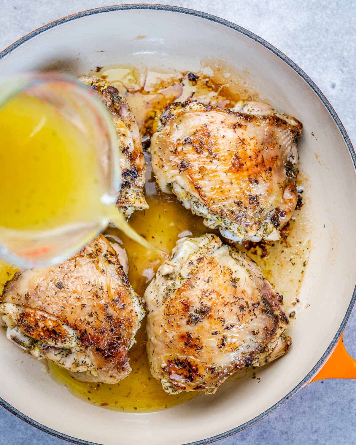 pouring chicken stock over chicken thighs in skillet 
