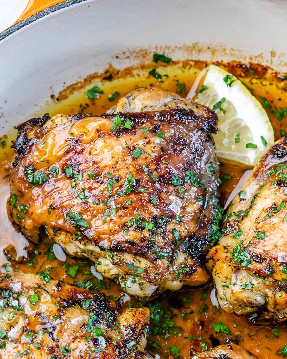 close up of a chicken thigh in skillet with parsley and lemon 