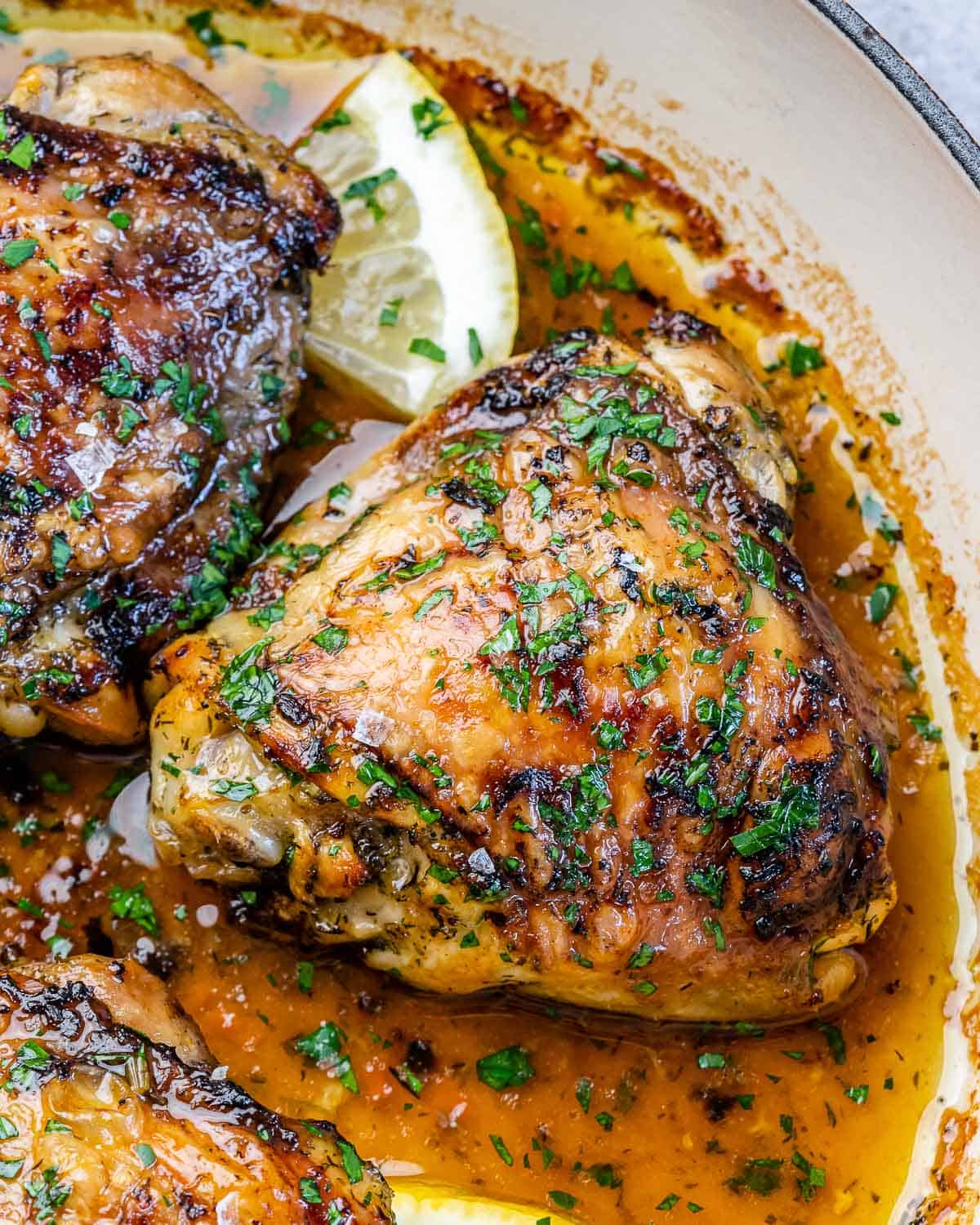 close view of baked chicken thighs with parsley and lemon wedges in skillet 