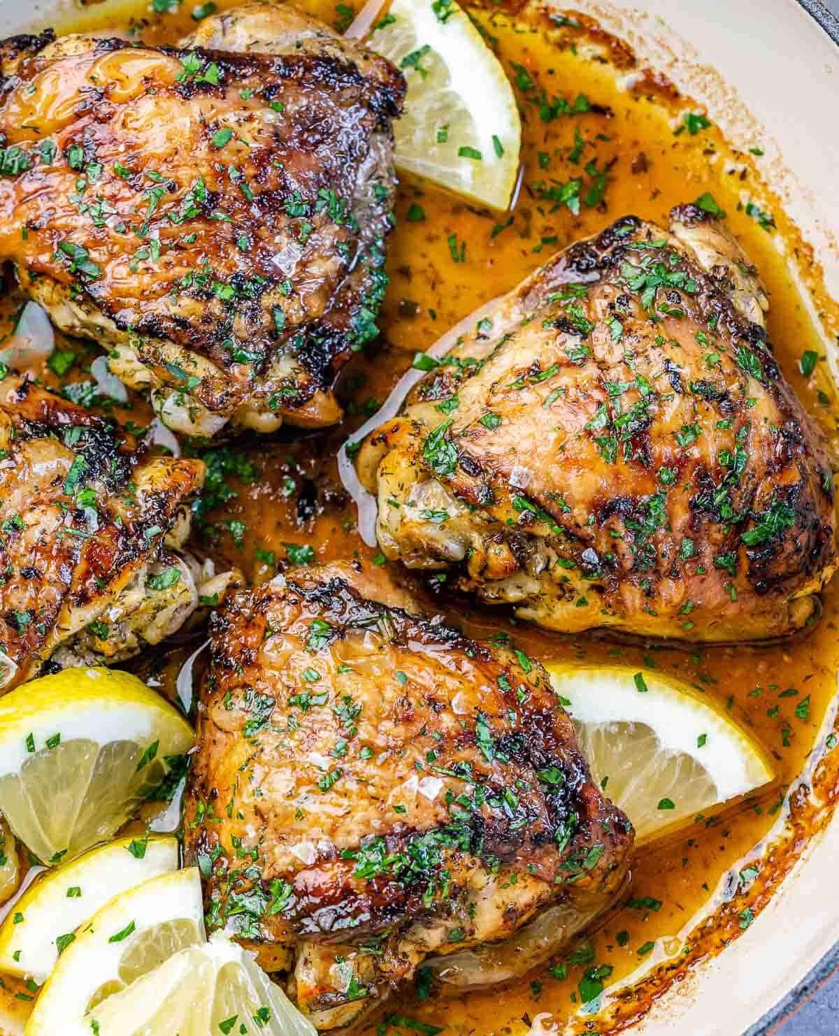 pan filled with baked chicken thighs garnished with lemon and parsey