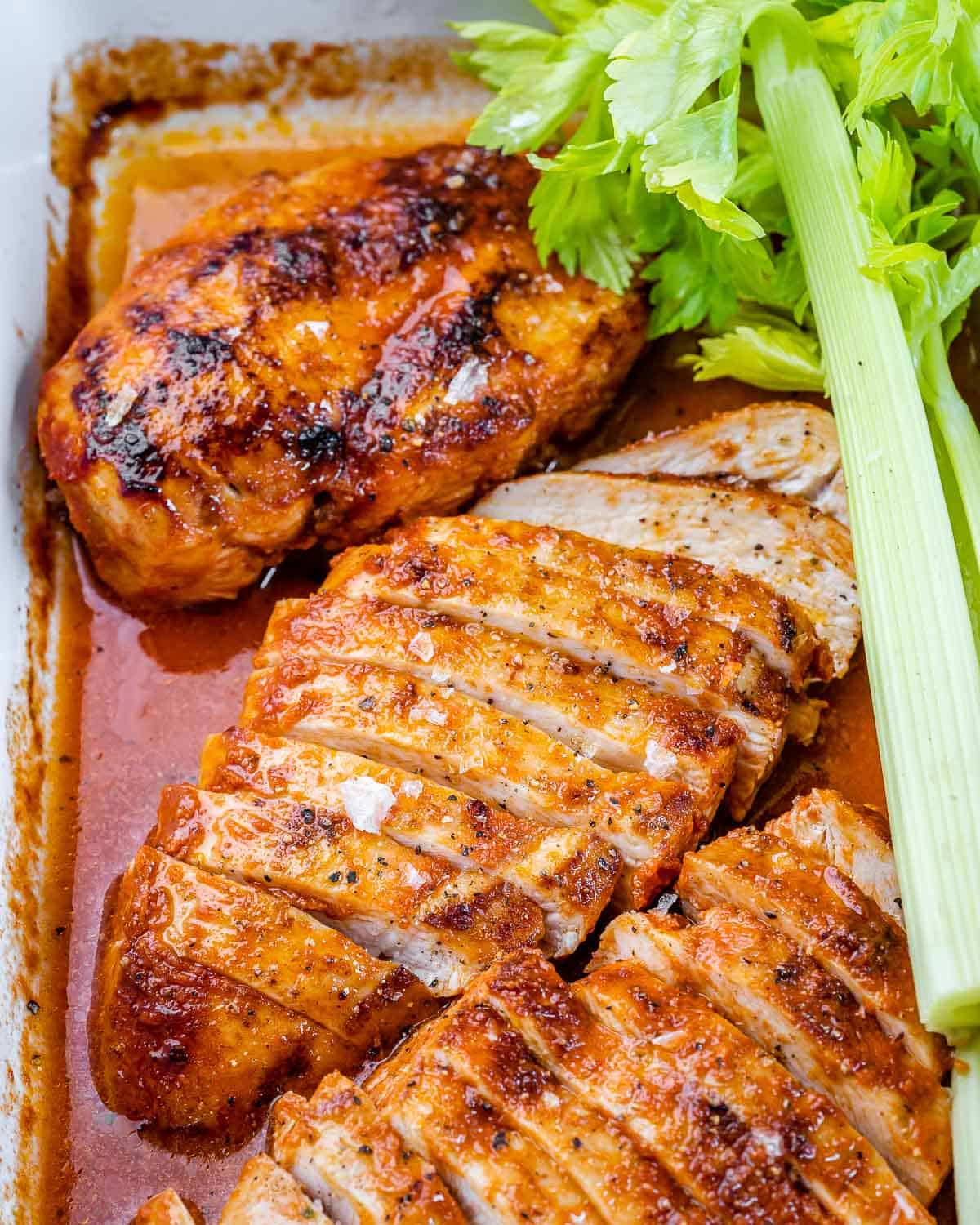 baked buffalo chicken breasts in dish with celery and buffalo sauce marinade