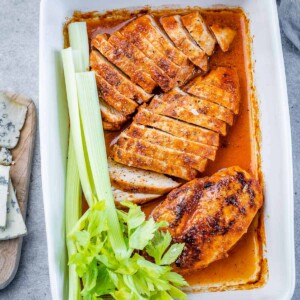 top view baked chicken breast with 2 chicken breast sliced in a baking dish and a celery stalk on the left of the chicken