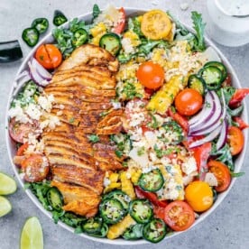 top view of arugula salad in a white bowl topped with sliced chicken breast and lime granishes