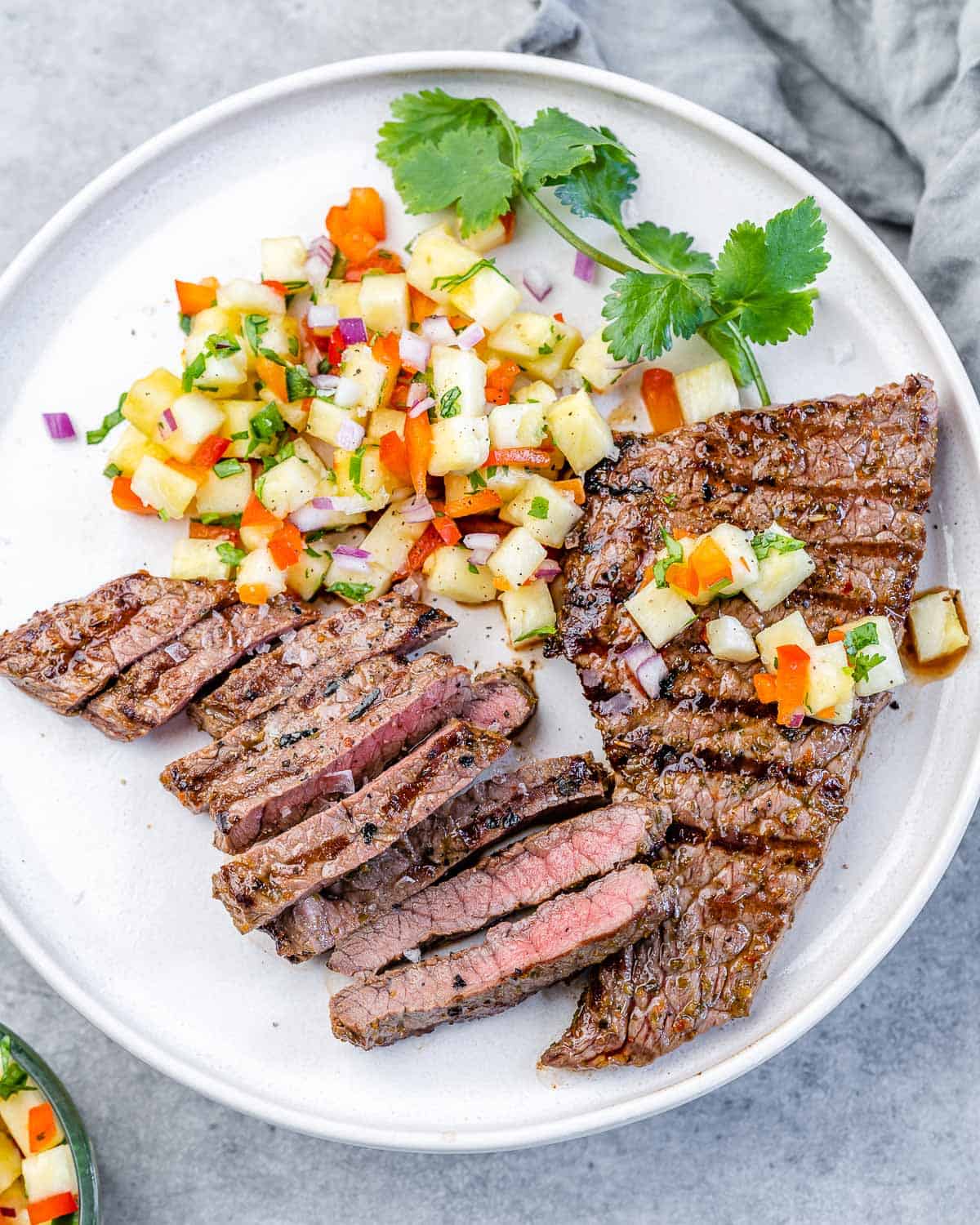 top view of grilled skirt steak on white plate with pineapple salsa