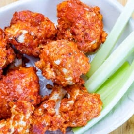 side shot of air fried bbq cauliflower wings in a white bowl with a side of celery sticks