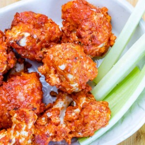 side shot of air fried bbq cauliflower wings in a white bowl with a side of celery sticks