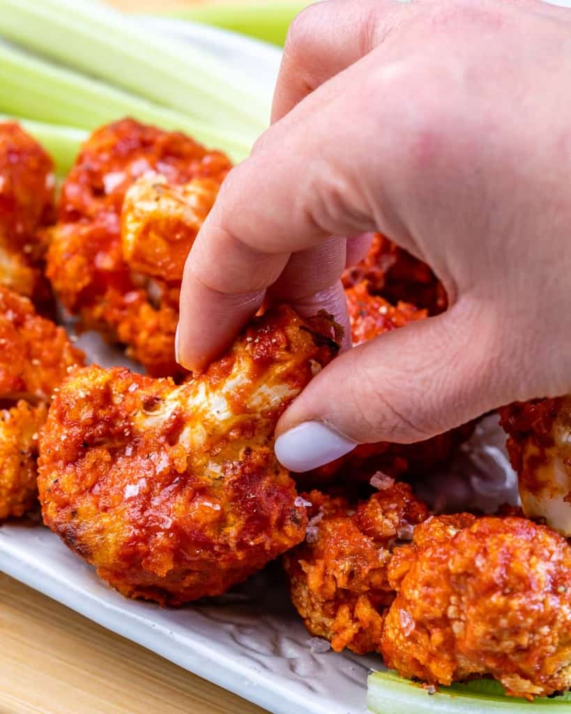 hand reaching for cauliflower wing from a plate 