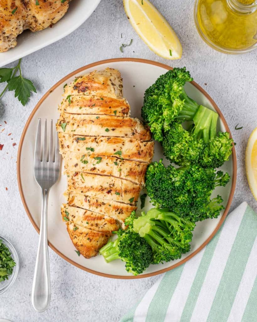 one chicken breast sliced on a white plate with a side of broccoli