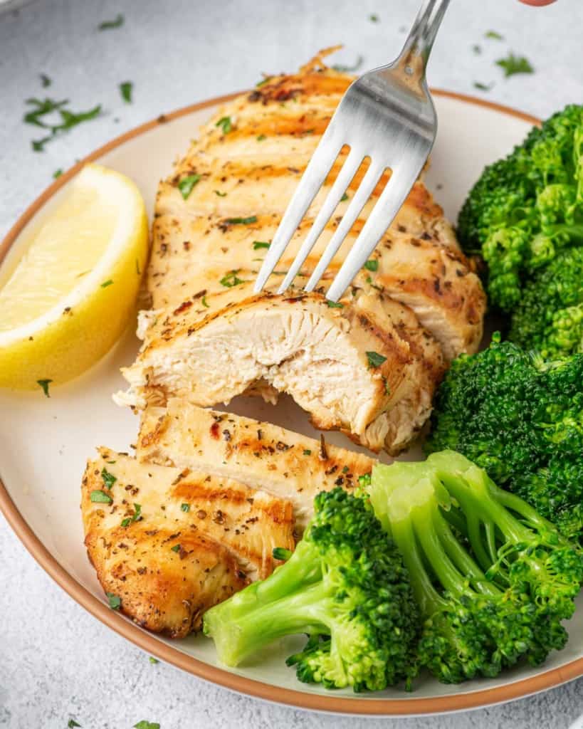 fork holding a slice of chicken breast on a plate with broccoli