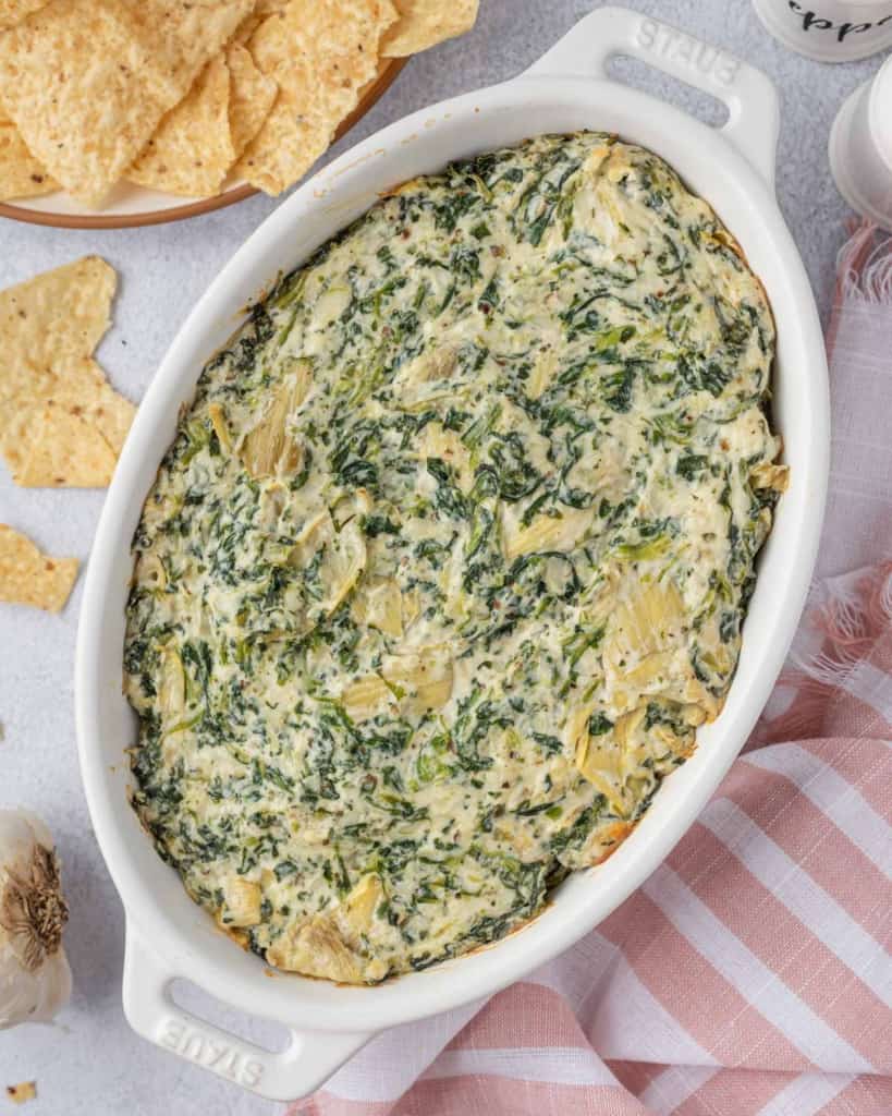 top view spinach and artichoke dip in a baking dish with a side of tortilla chips 