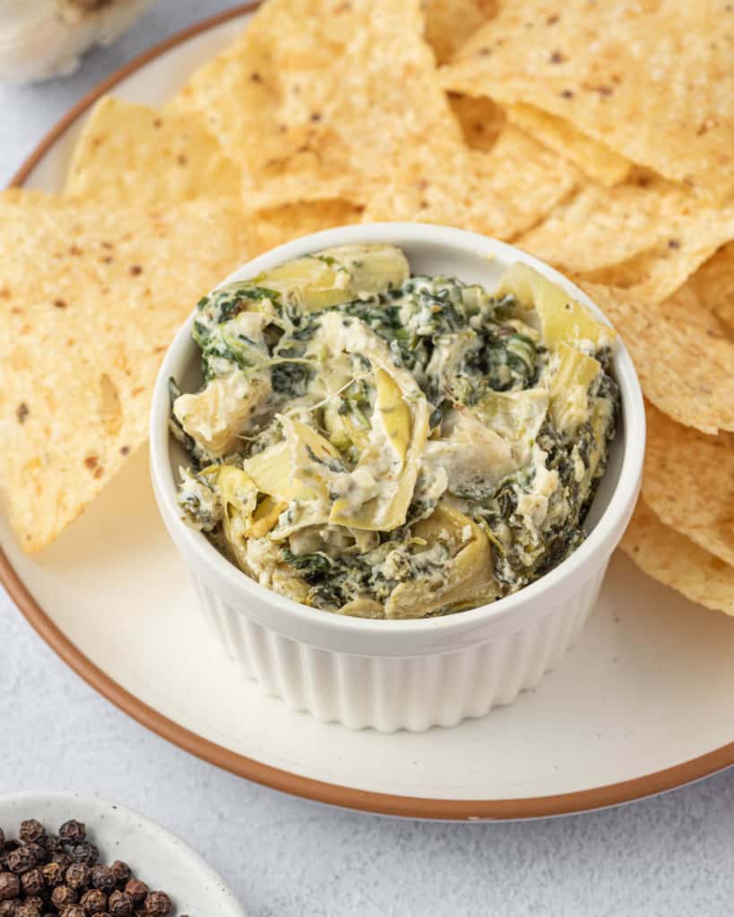 side shot of artichoke dip in a bowl served with tortilla chips 