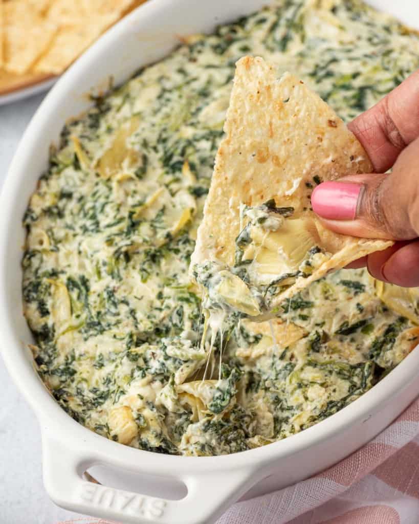 hand holding chips scooping artichoke dip