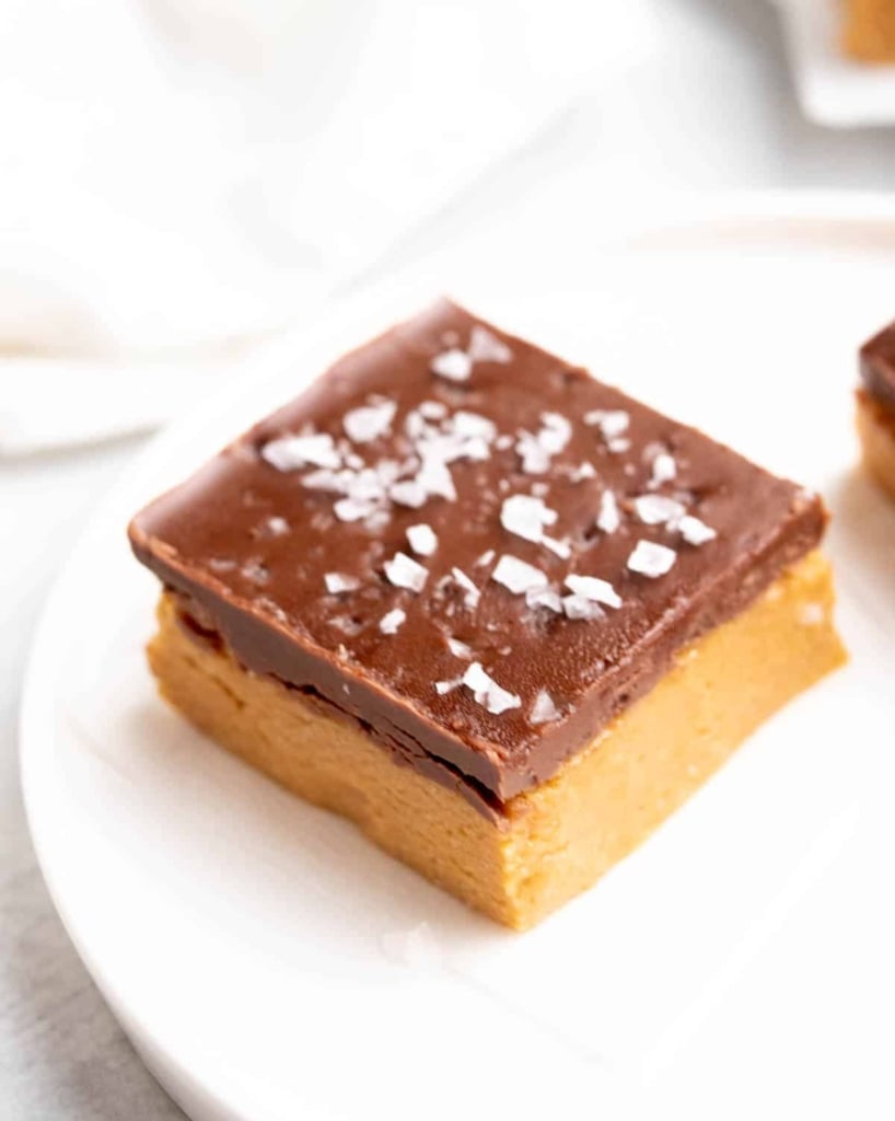 side shot of peanut butter bar on a white plate topped with salt flakes