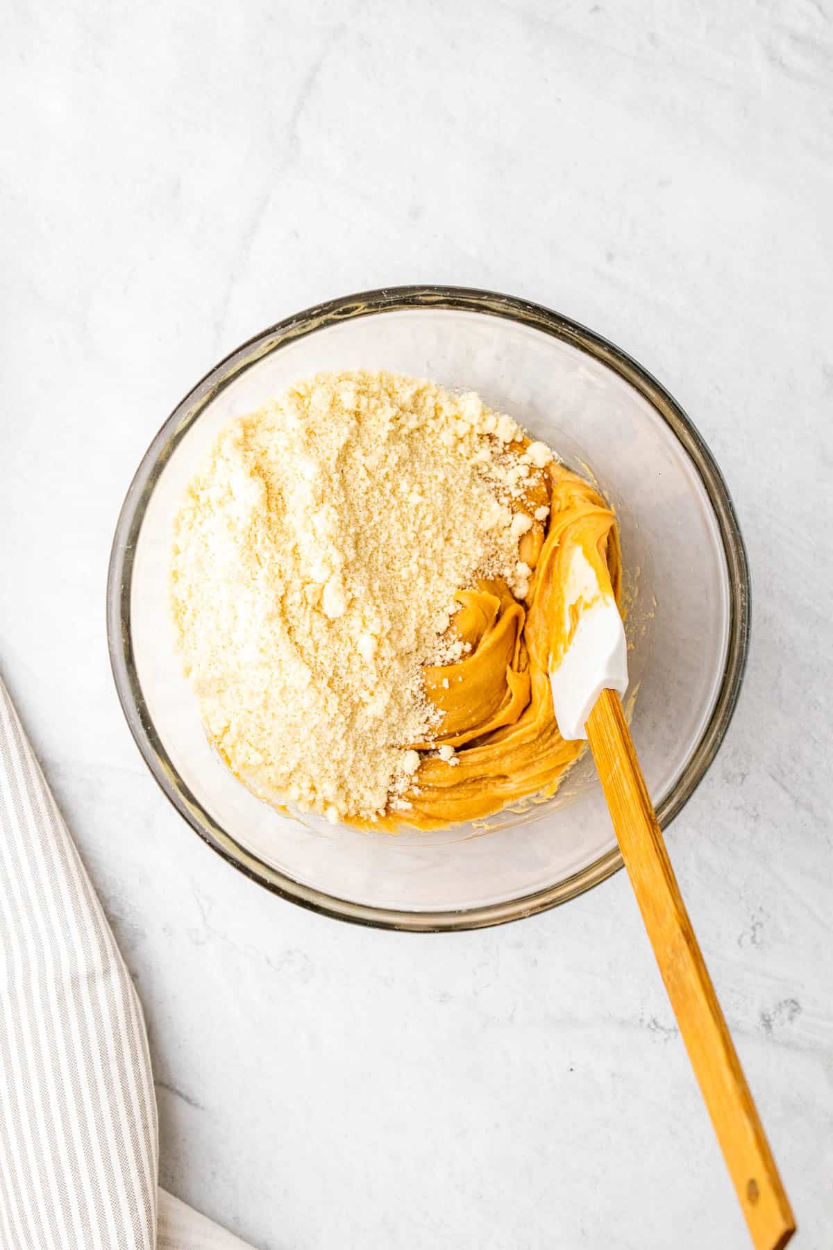 Flour added to peanut butter mixture in a clear bowl with a spatula.