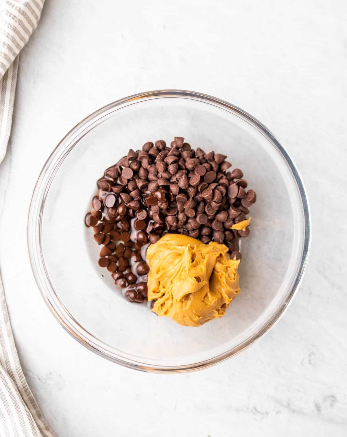 peanut butter added over chocolate chips in a clear bowl