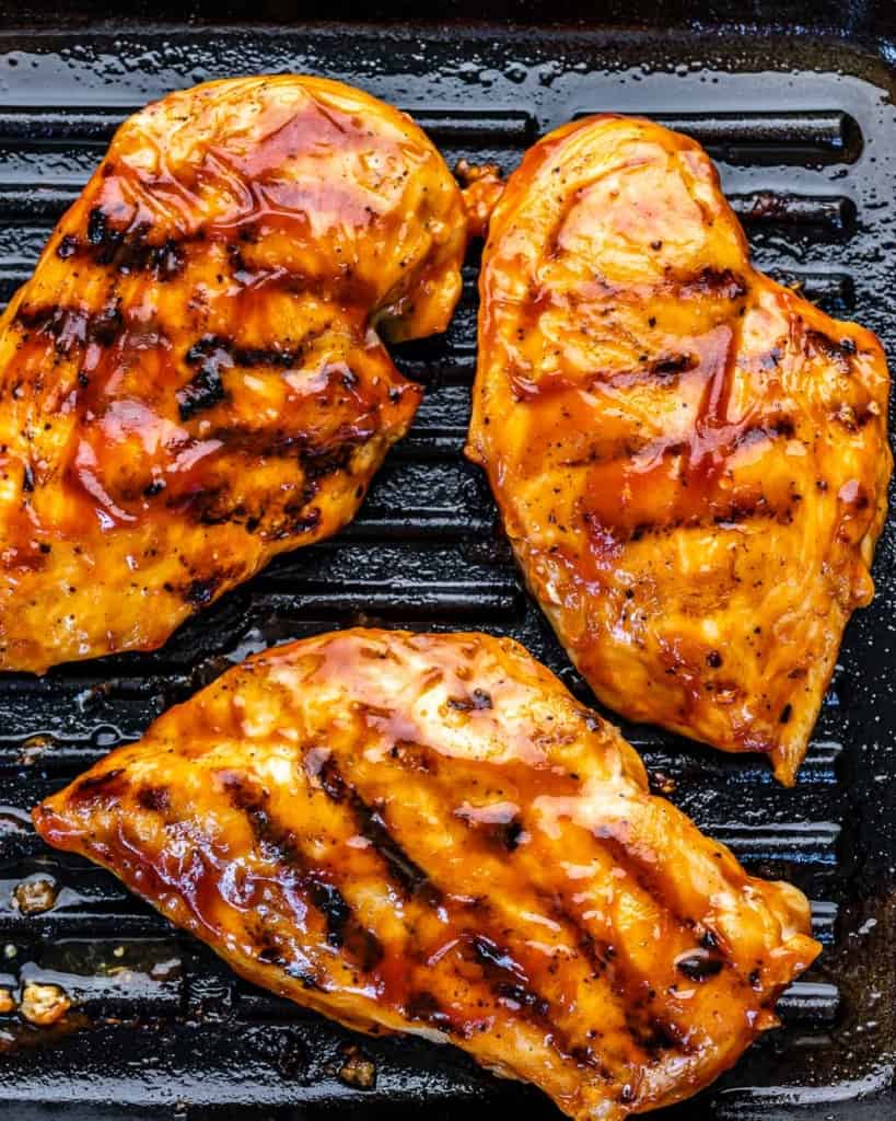 four BBQ chicken breasts on grill pan with barbecue sauce