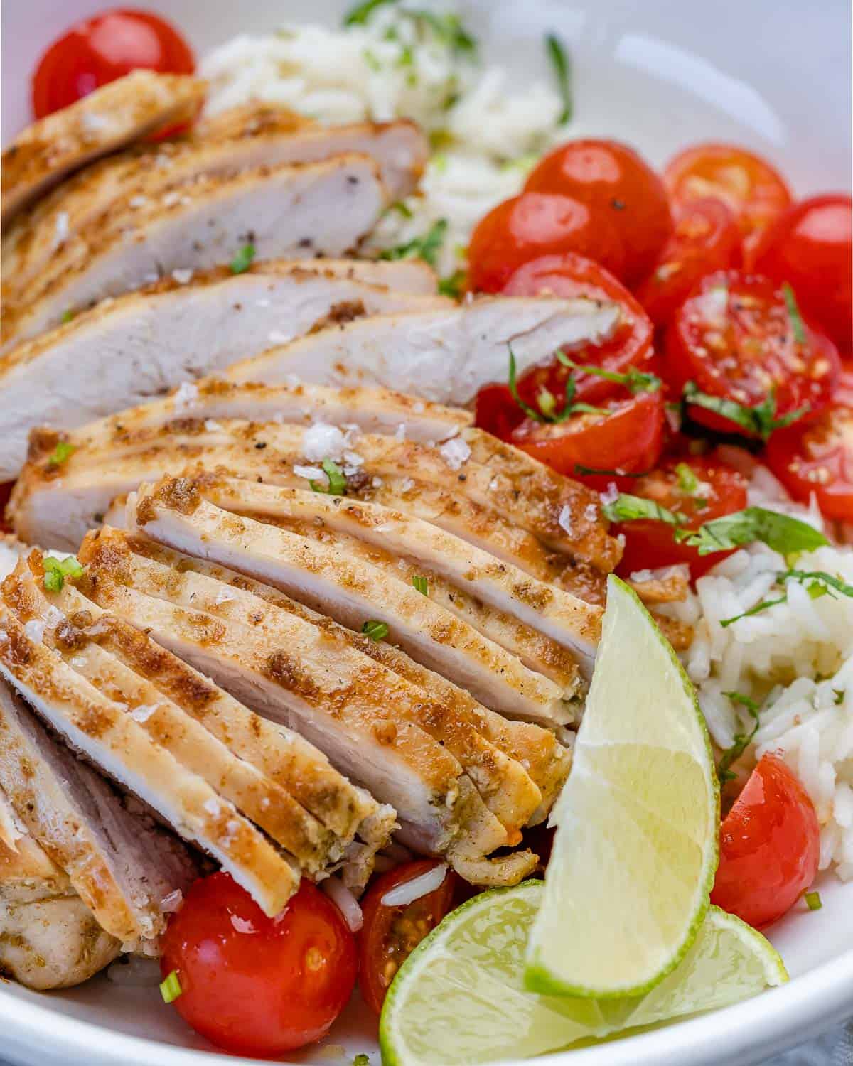 front view of chicken sliced over cilantro rice with tomatoes and lime wedges