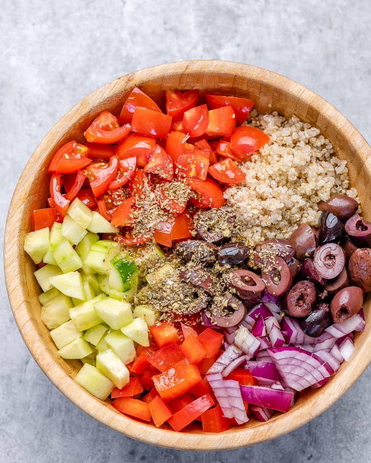 cucumbers, tomatoes, red onion, kalamata olives, quinoa, and oregano in bowl 