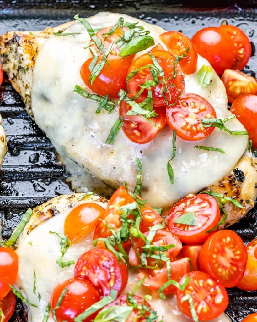 side shot of grilled chicken breast with cheese and tomatoes 