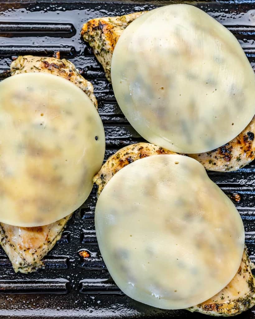 Cheese on top of Grilled Chicken on a black grill pan.
