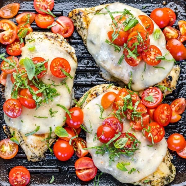 top view grilled chicken topped with melted cheese, sliced cherry tomatoes, and basil, all in a grill pan