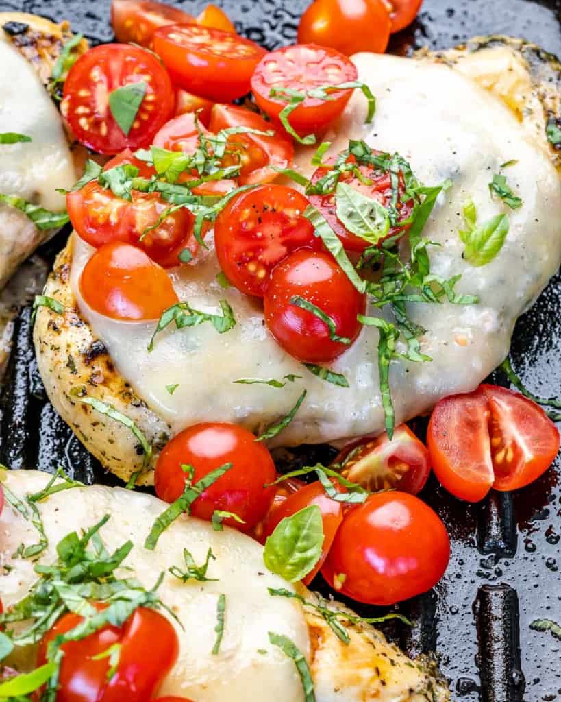 close up grilled chicken breast topped with cheese and chopped tomatoes 