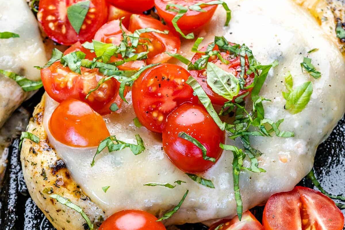 close up grilled chicken breast topped with cheese and chopped tomatoes