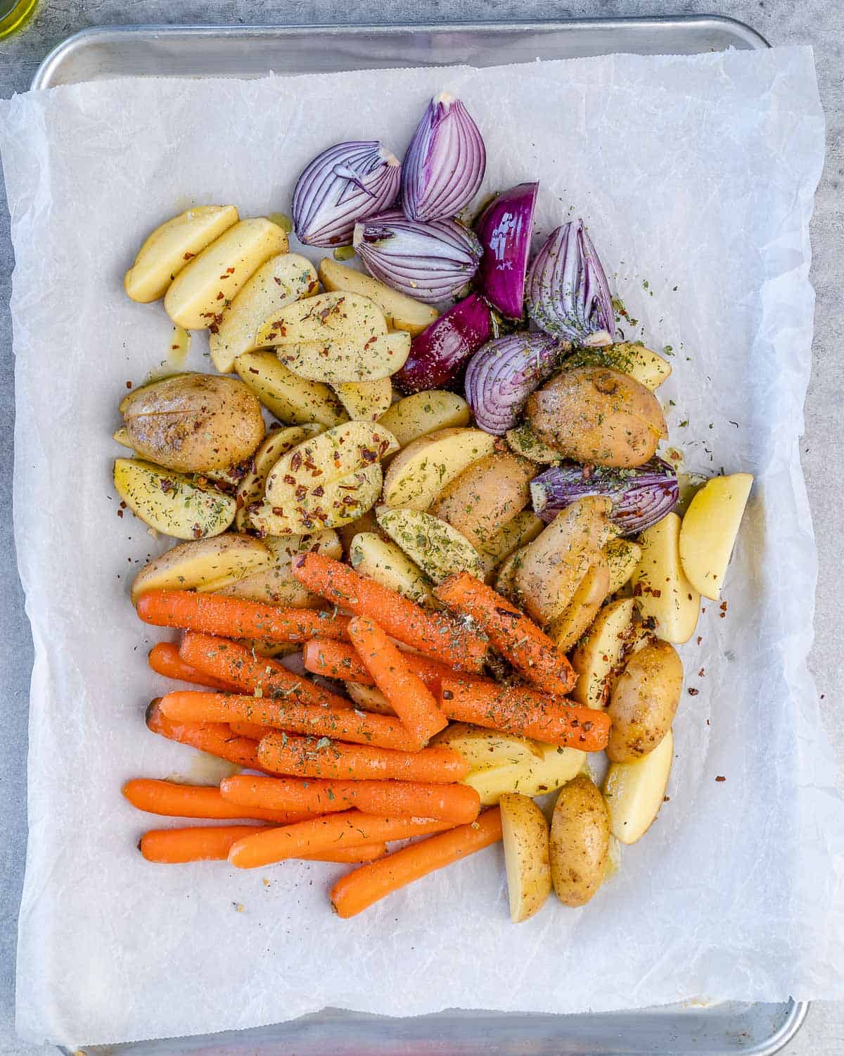 onions, carrots, and potatoes on baking sheet with parchment paper topped with seasoning
