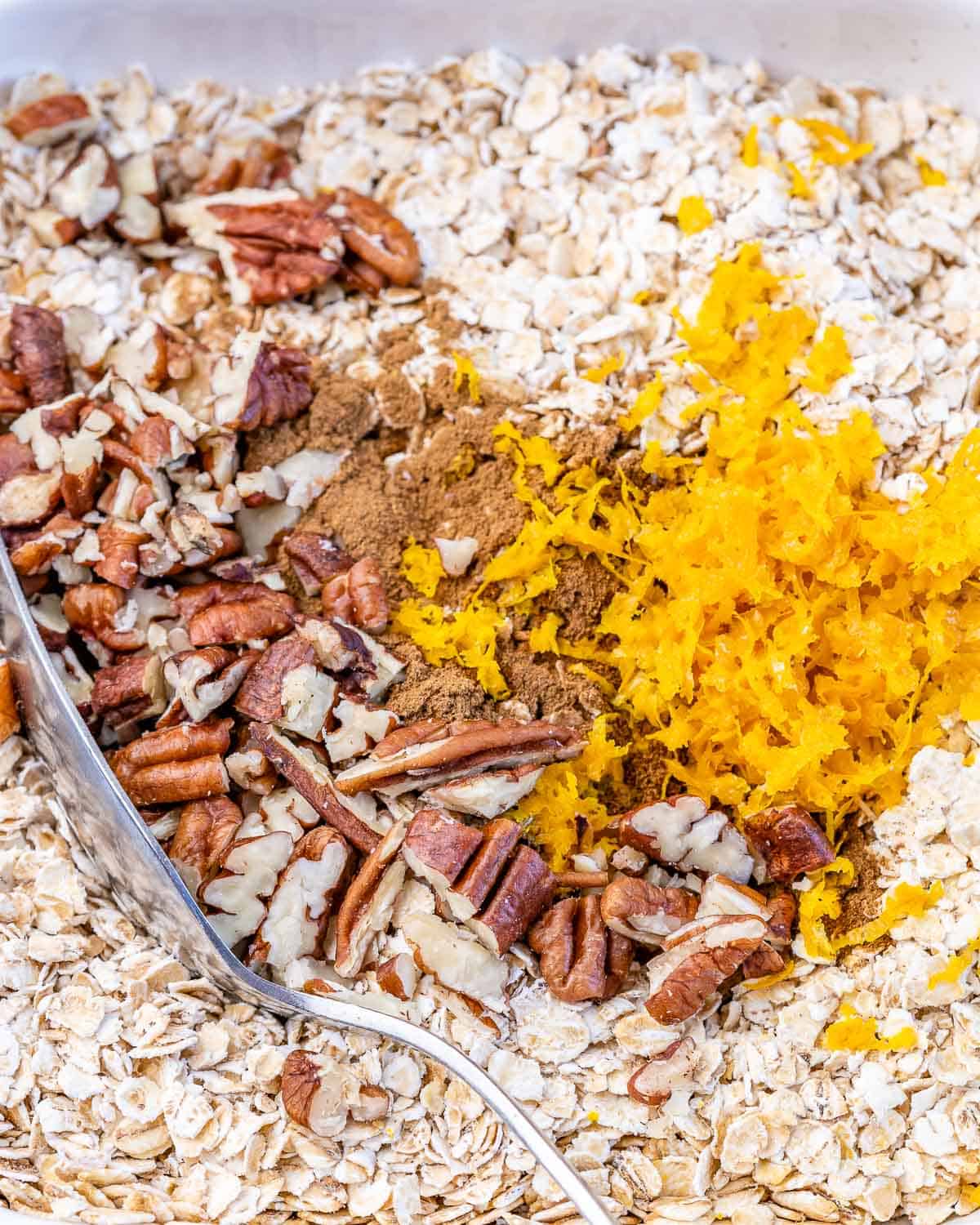 mixing oats with pecans, orange zest, maple syrup, milk, in bowl 