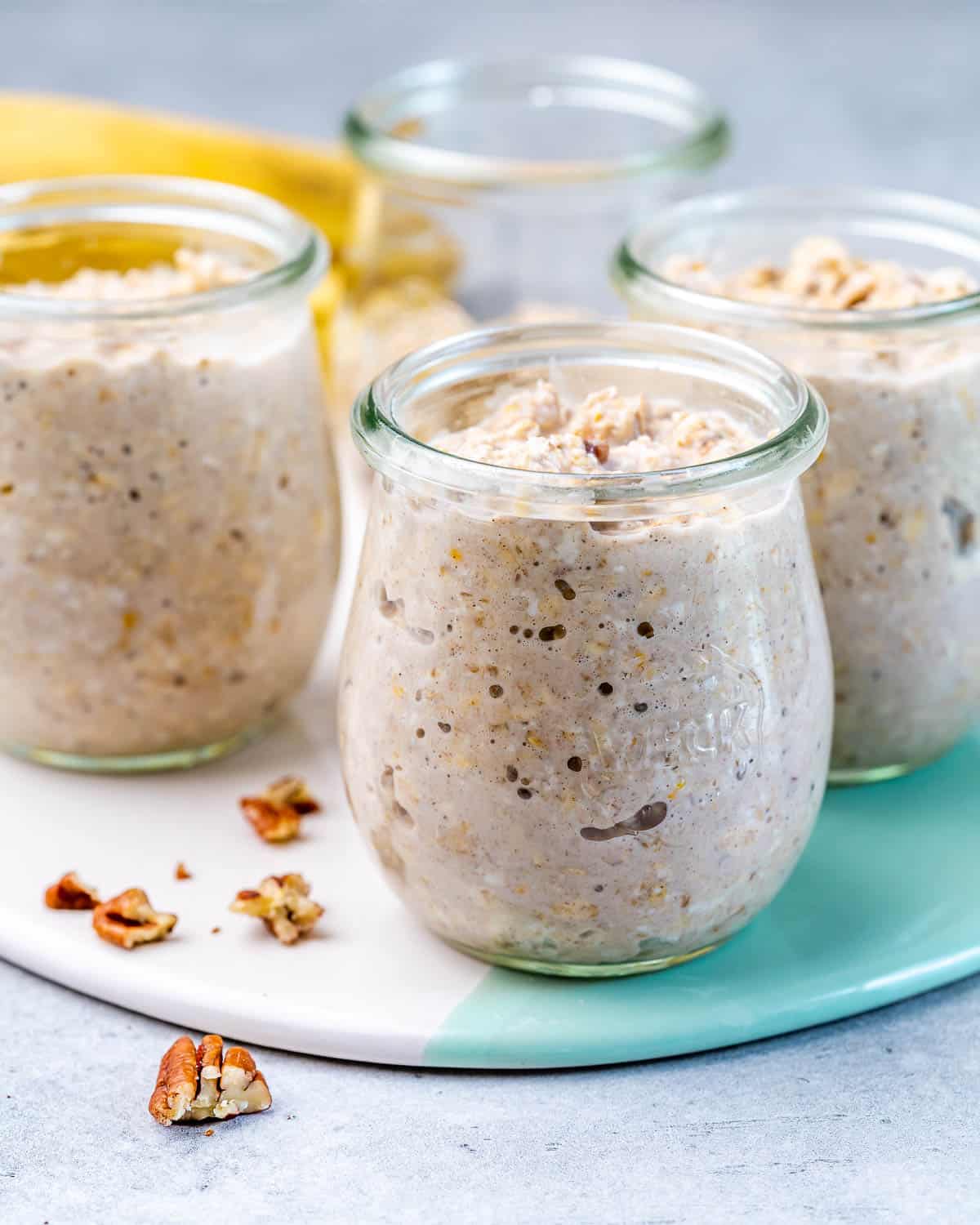 pouring overnight oats into four jars with pecans and mashed bananas 