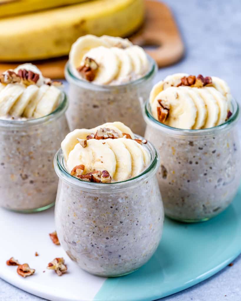 overnight oats with banana in four jars topped with pecans