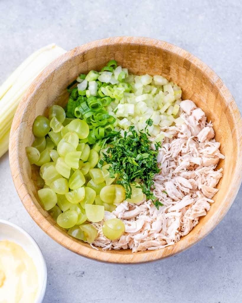 Shredded chicken, grapes, celery, onion and parsley added to a bowl.