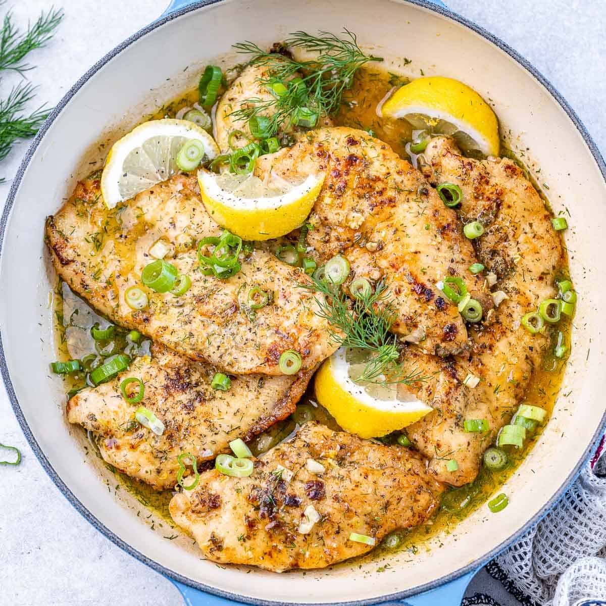 top view lemon chicken breasts in a white pan with lemon garnishes